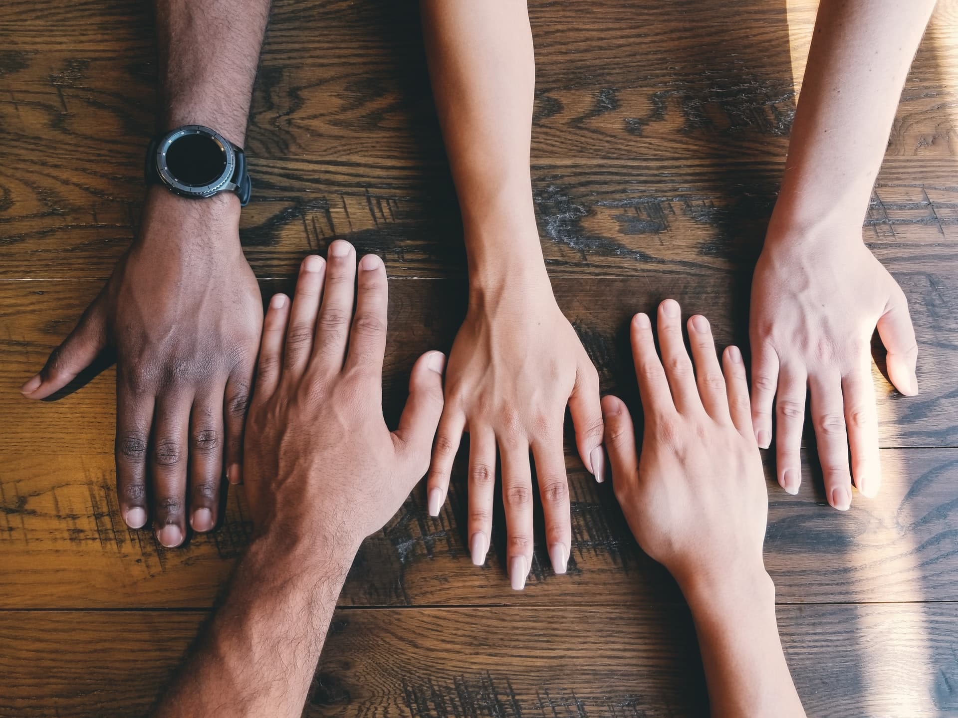 Image shows hands of different ethnicities resting on a table, illustrating the concept of diverse hires.