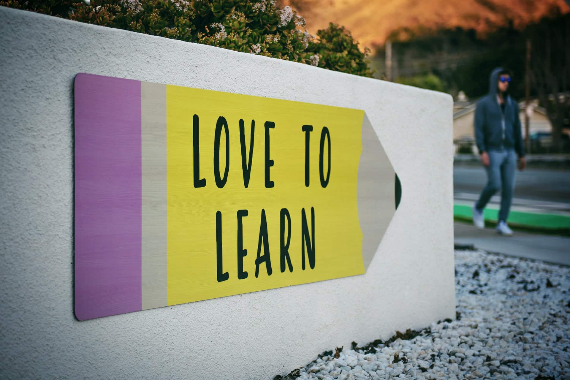 The image shows a “Love to Learn” pencil signage on a wall near a walking man to illustrate the concept of personal development topics.