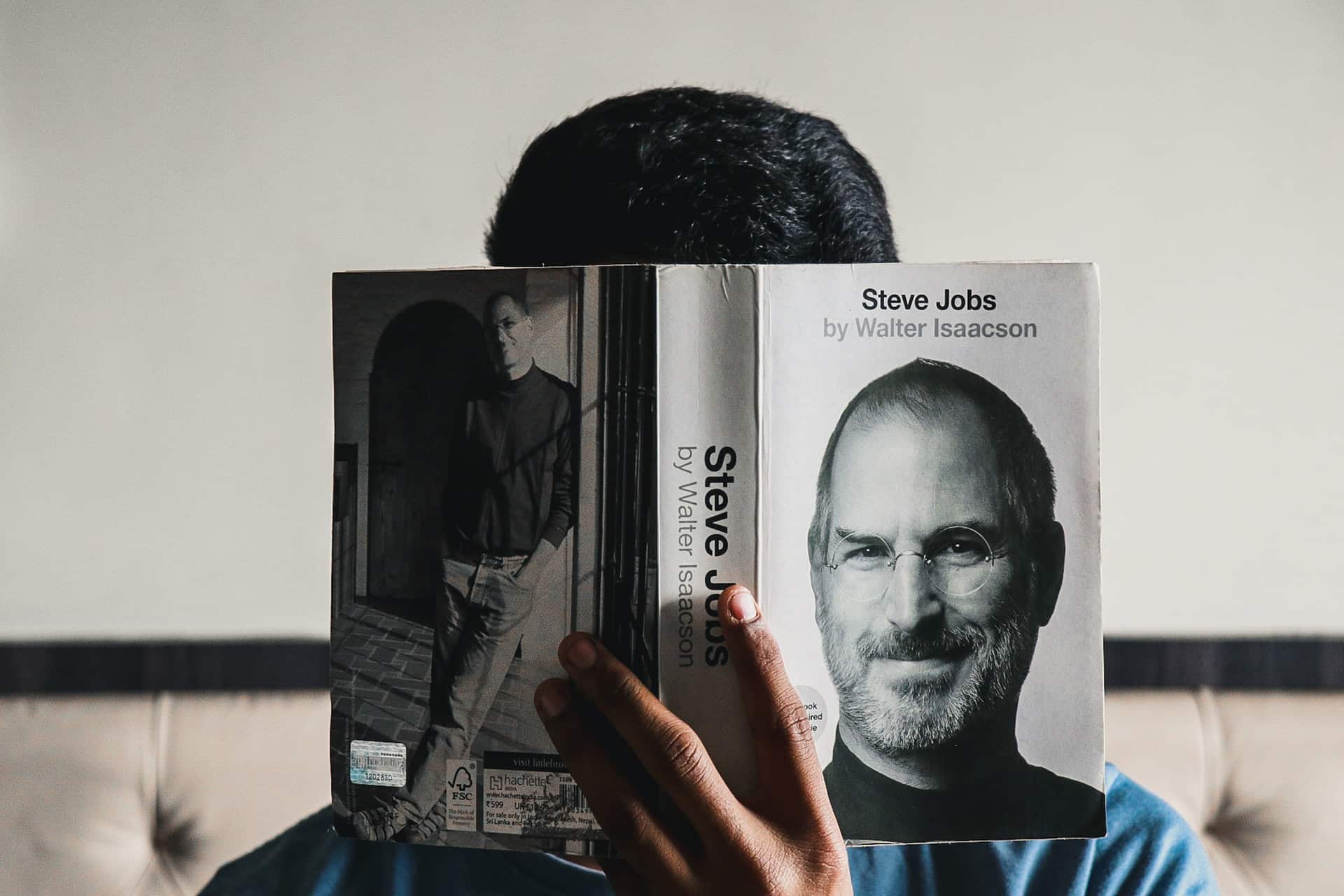 A man reads a book. We see on the cover of the book Steve Jobs.