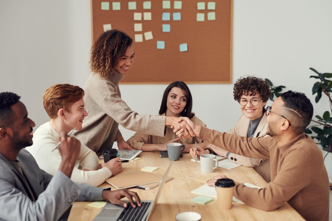 A group of people in a business meeting. A woman is shaking hands with a man celebrating the success to keep the balance between entrepreneur and intrapreneur.