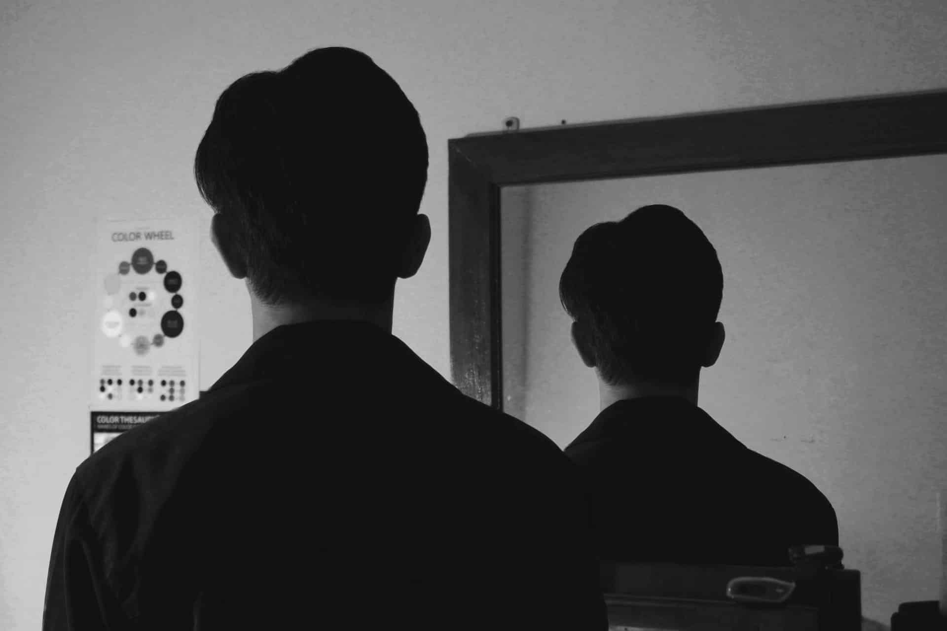 We see a person who stands in front of a mirror. We can only see his back in the picture. Also, the reflection in the mirror shows his back. What are the personality traits of this person?