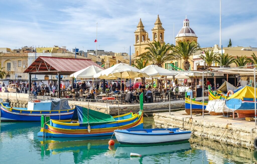 Old port of Valletta in Malta with boats and blue sea, with church in the background